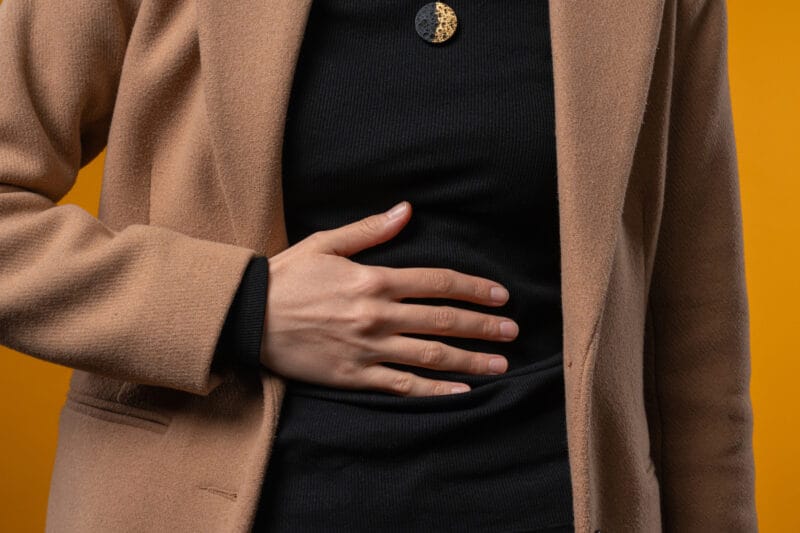 A person in a brown coat with a hand over their stomach.