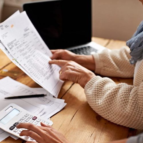 Two people reviewing financial documents at a desk with a calculator and laptop.