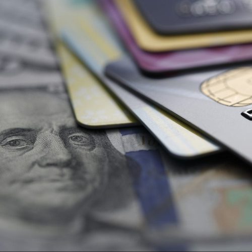 A close-up image of several credit cards stacked on top of U.S. hundred-dollar bills.