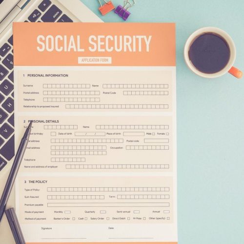 A Social Security application form on top of a laptop, on a desk with a cup of coffee and pens nearby.