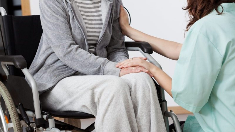 ​​Caregiver comforting a person in a wheelchair, holding their hand and offering support.