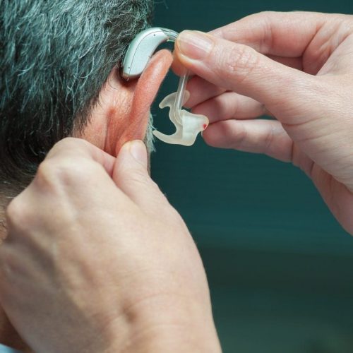 Close-up of a person being fitted with a behind-the-ear hearing aid by a medical professional.