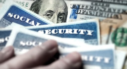A stack of social security cards on top of a $100 bill.