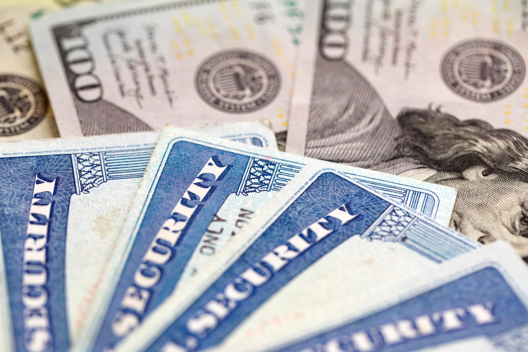 Close up of four social security cards on top of $100 bills