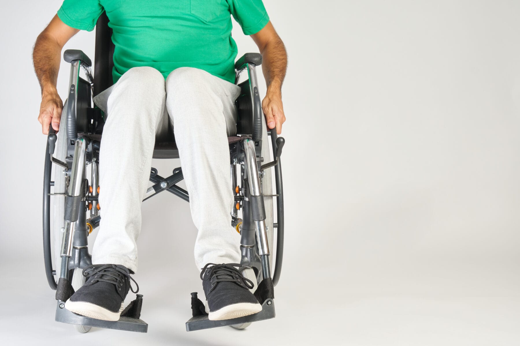 A person in a wheelchair wearing a green shirt and light-colored pants, positioned against a plain background.
