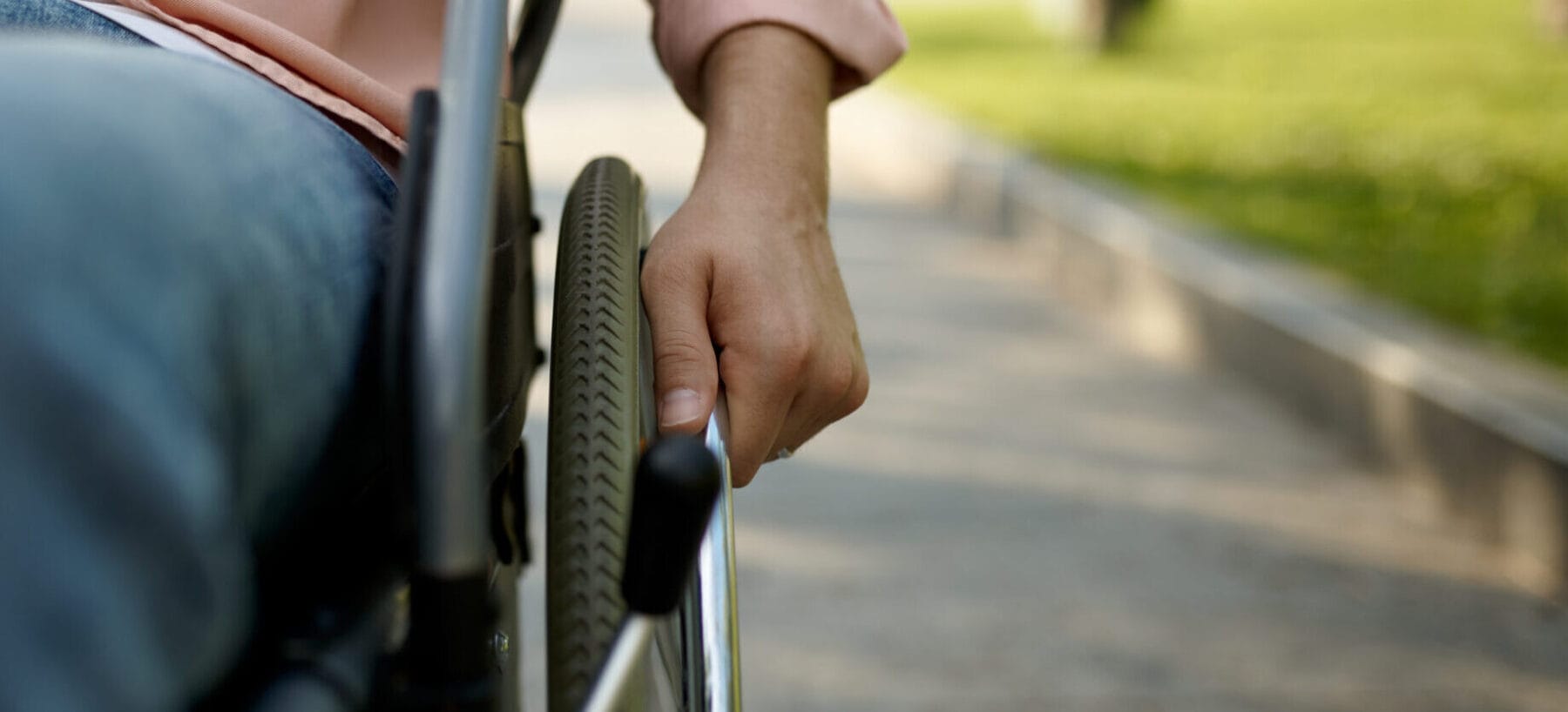 Close up of a man on a sidewalk with his hand on the wheel of his wheelchair.