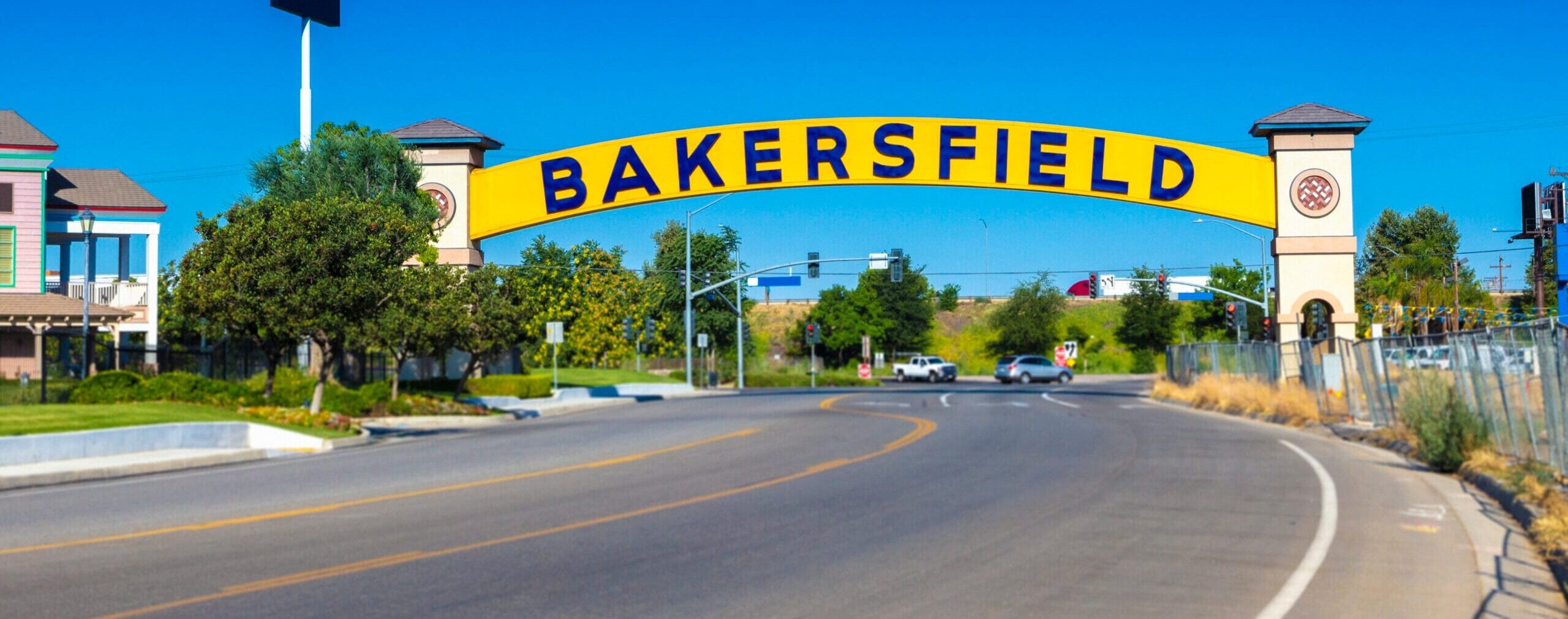 The yellow and blue Bakersfield arch stretching over a sunny street with trees, cars, and clear blue skies in Bakersfield, California.