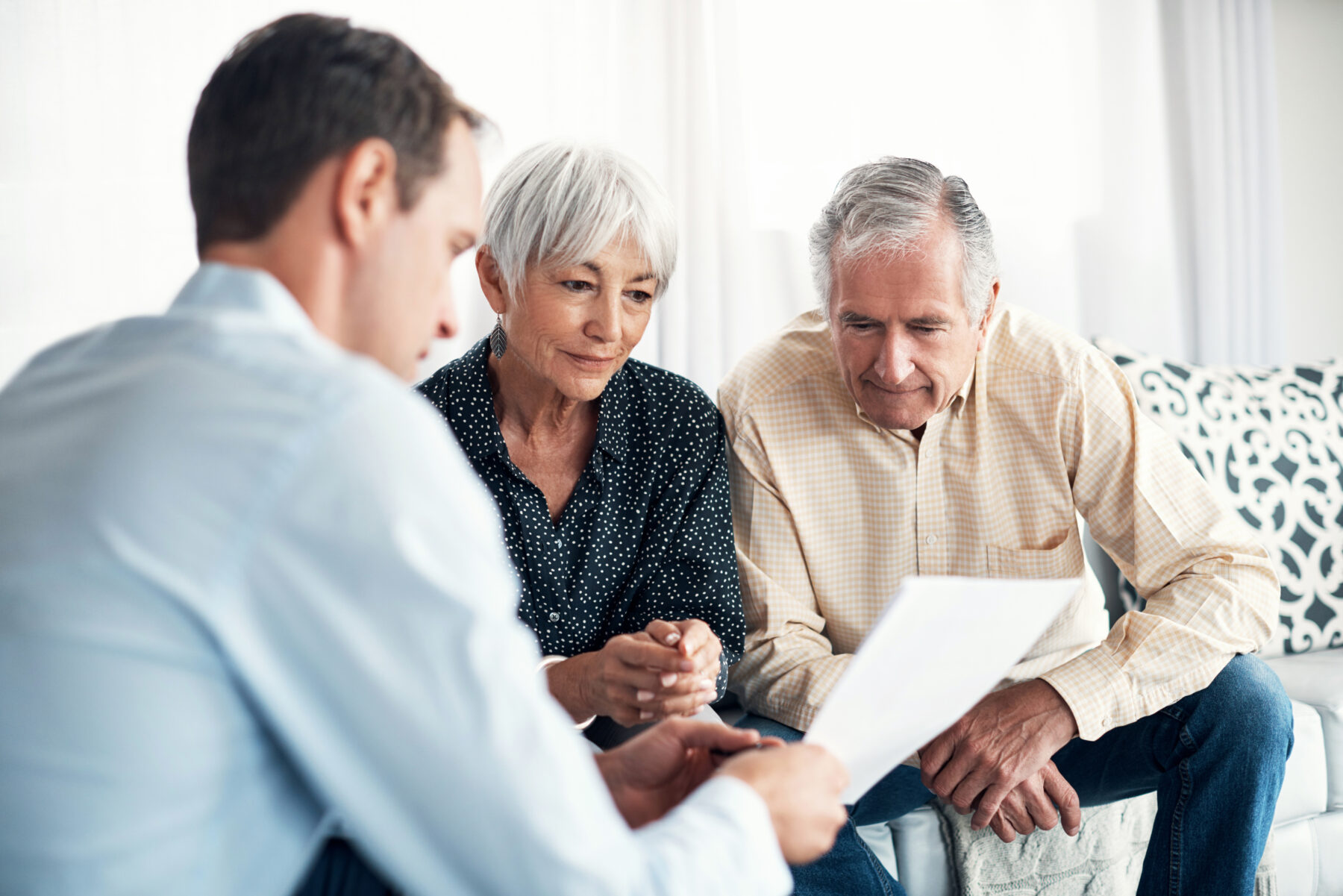 A man shows documents to an older couple sitting together on a couch, reviewing paperwork.