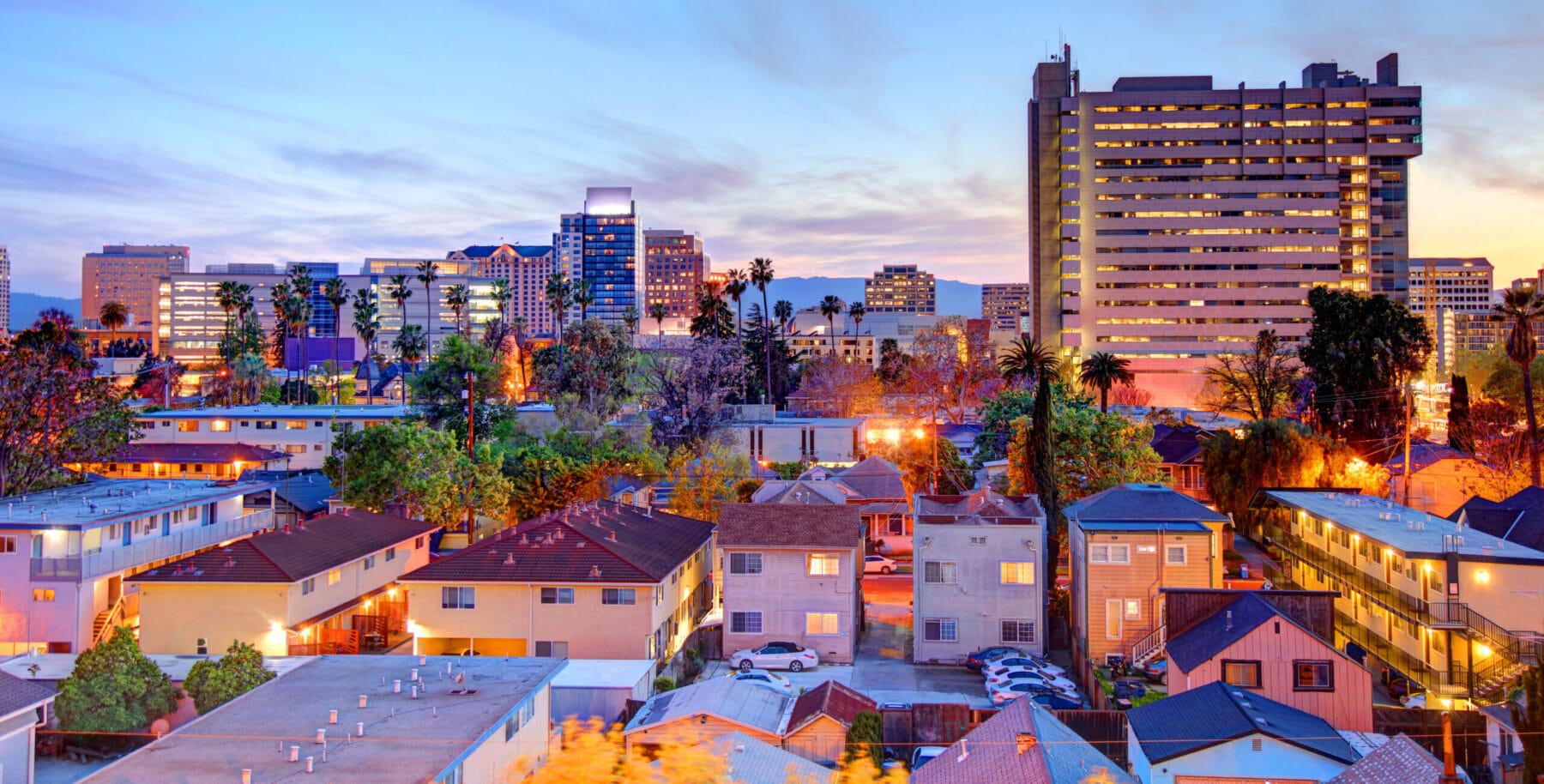Cityscape of San Jose, California at sunset, featuring downtown buildings and residential neighborhoods.
