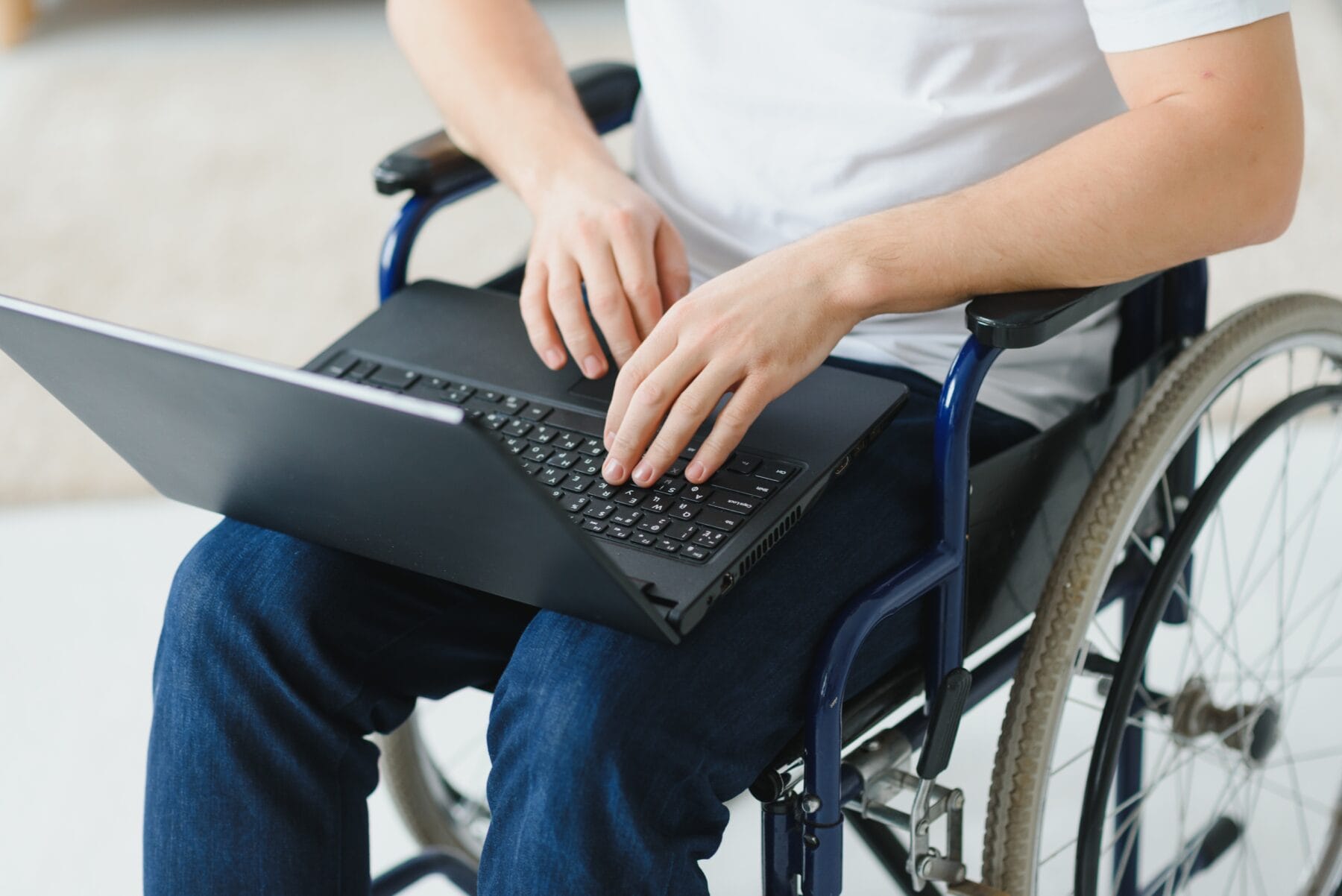 Close up of a man using a laptop while seated in a wheelchair.